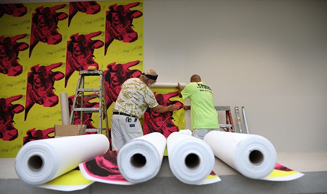 Workers at the Memorial Art Gallery hang cow wallpaper that is part of the "Season of Warhol" exhibit. - PHOTO BY MAX SCHULTE