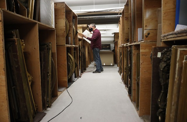 The Rochester Historical Society archivist Bill Keeler sifts through old painting and drawings of locals collected over the years. The new location doesn't have wall space to hang all the works in wood stacks. - PHOTO BY MAX SCHULTE