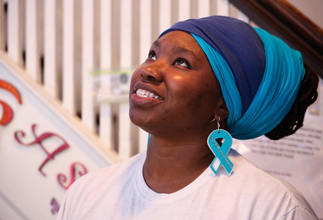 BeRana Divine, who was diagnosed with cervical cancer in July 2021, wears teal and white earrings engraved with the word "Surviving." - PHOTO BY MAX SCHULTE